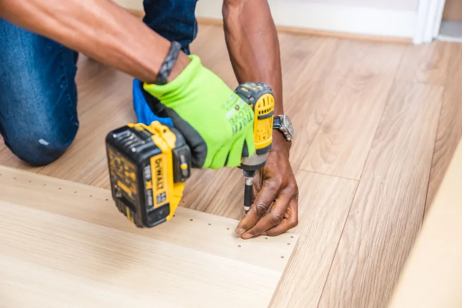 Installer kneeling on a pale plank floor, fastening a board in a customer's home
